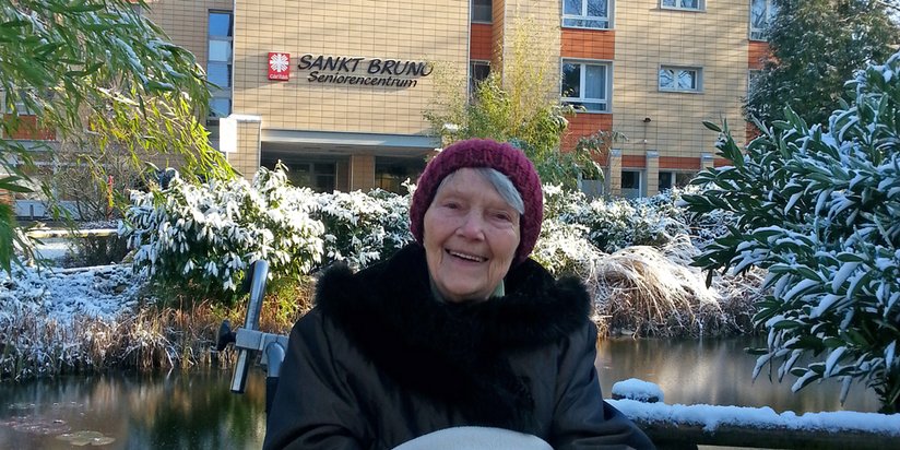 Eine ältere Dame sitzt im winterlichen Garten vor dem Seniorencentrum 